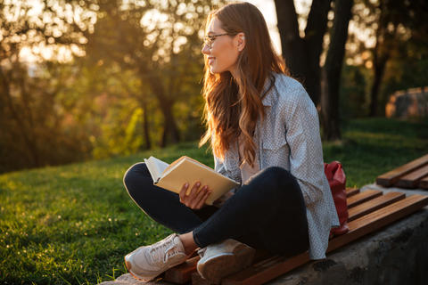 Frau sitzt draußen in der Sonne mit einem Buch